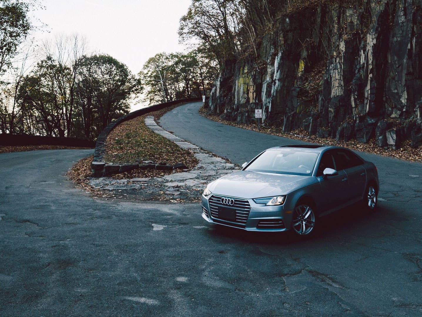 Silver Audi A4 on a winding mountain road with dramatic rock face and autumn foliage